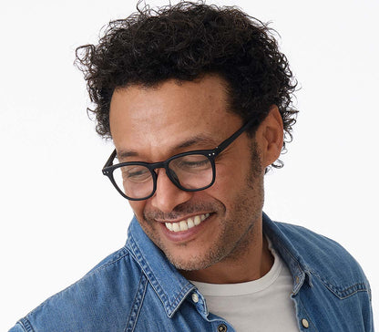 Male model wearing Scholar (Black) retro unisex reading glasses with large oval shaped lenses, slender black frames and rivet details.