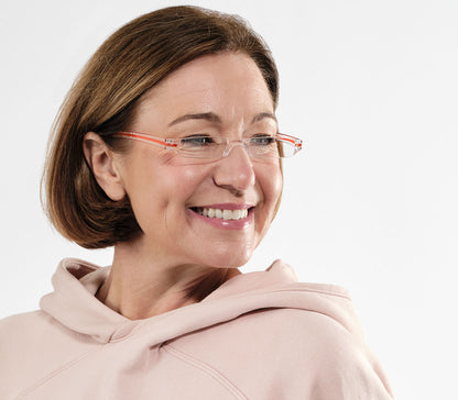 Female model wearing Soda (Orange) sleek, compact and ultra lightweight reading glasses with clear frames and orange detailed temples.