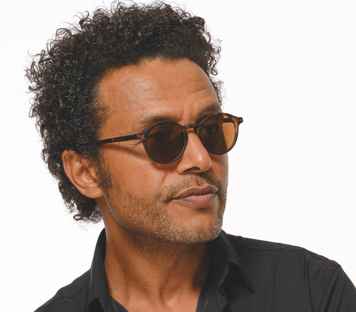 Male model wearing Modena (Tortoiseshell) round lens retro sunglasses with a slender, dark tortoiseshell frame and brown tinted lenses.